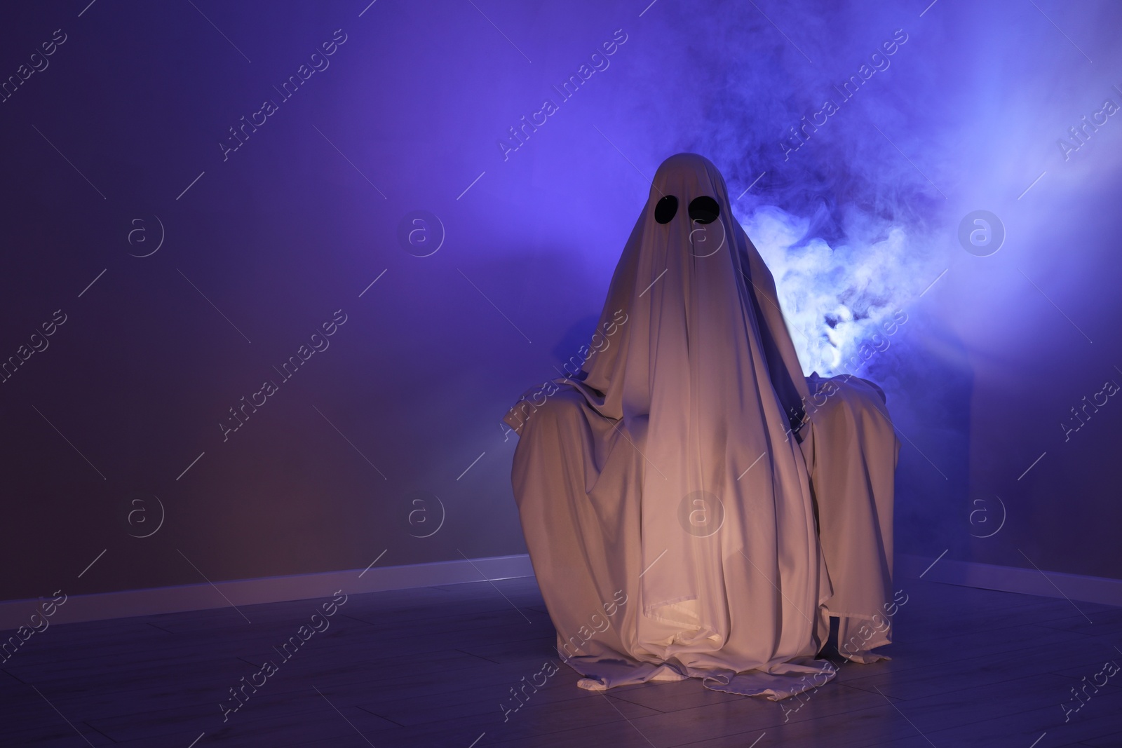 Photo of Creepy ghost. Woman covered with sheet sitting in armchair in blue light, space for text