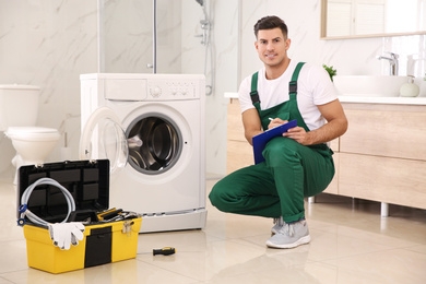 Photo of Repairman with clipboard and toolbox near washing machine in bathroom