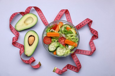 Photo of Measuring tape, salad and halves of avocado on light background, flat lay