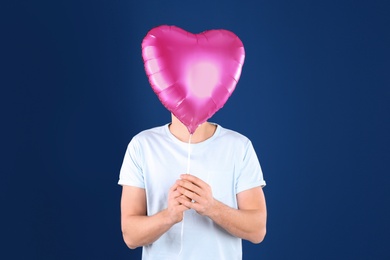 Photo of Young man with heart shaped balloon on color background