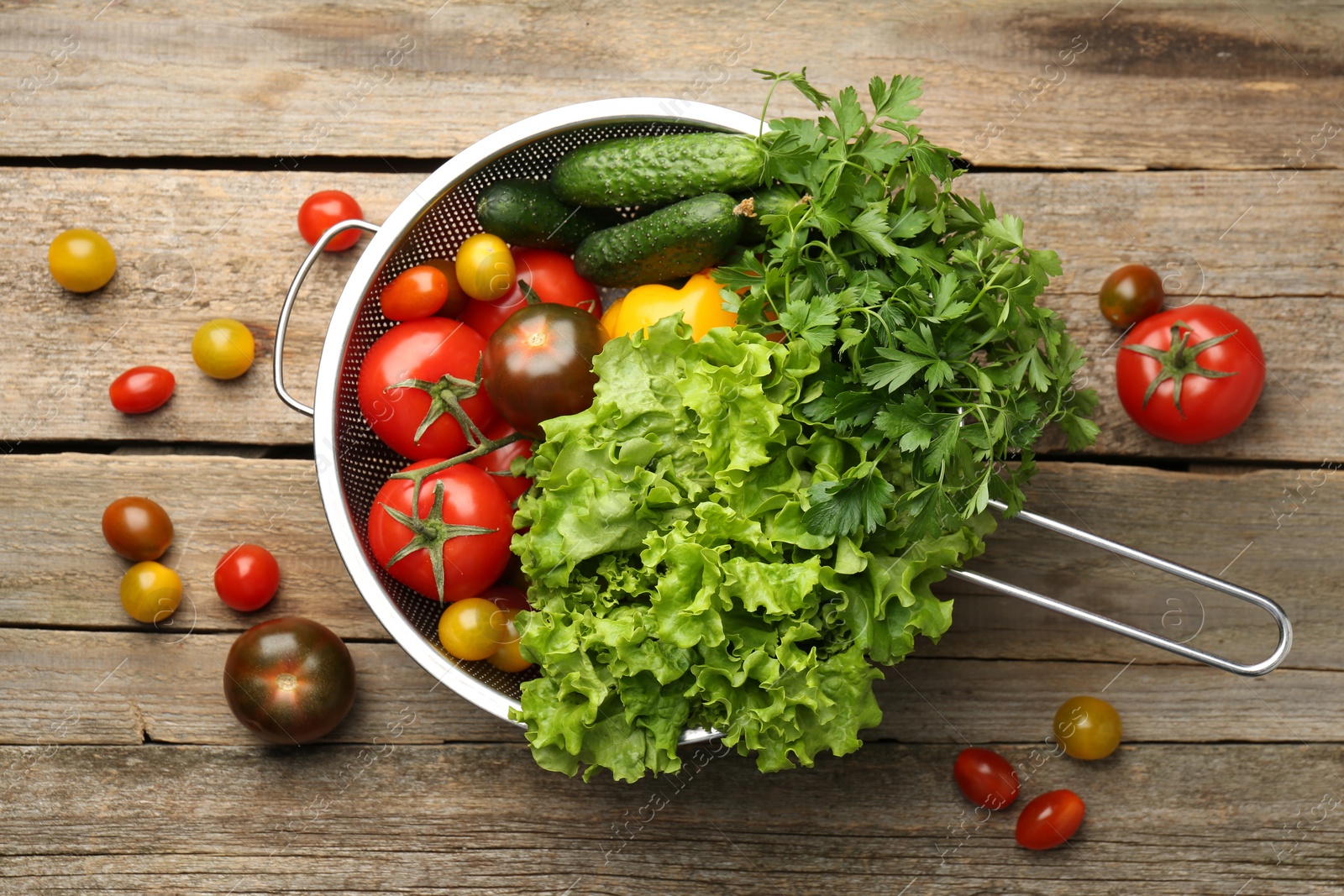 Photo of Fresh vegetables in colander on wooden table, flat lay