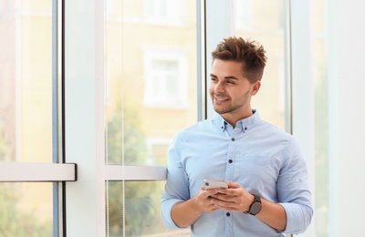 Photo of Portrait of handsome young man with smartphone near window