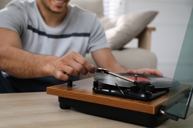Man using turntable at wooden table indoors, closeup