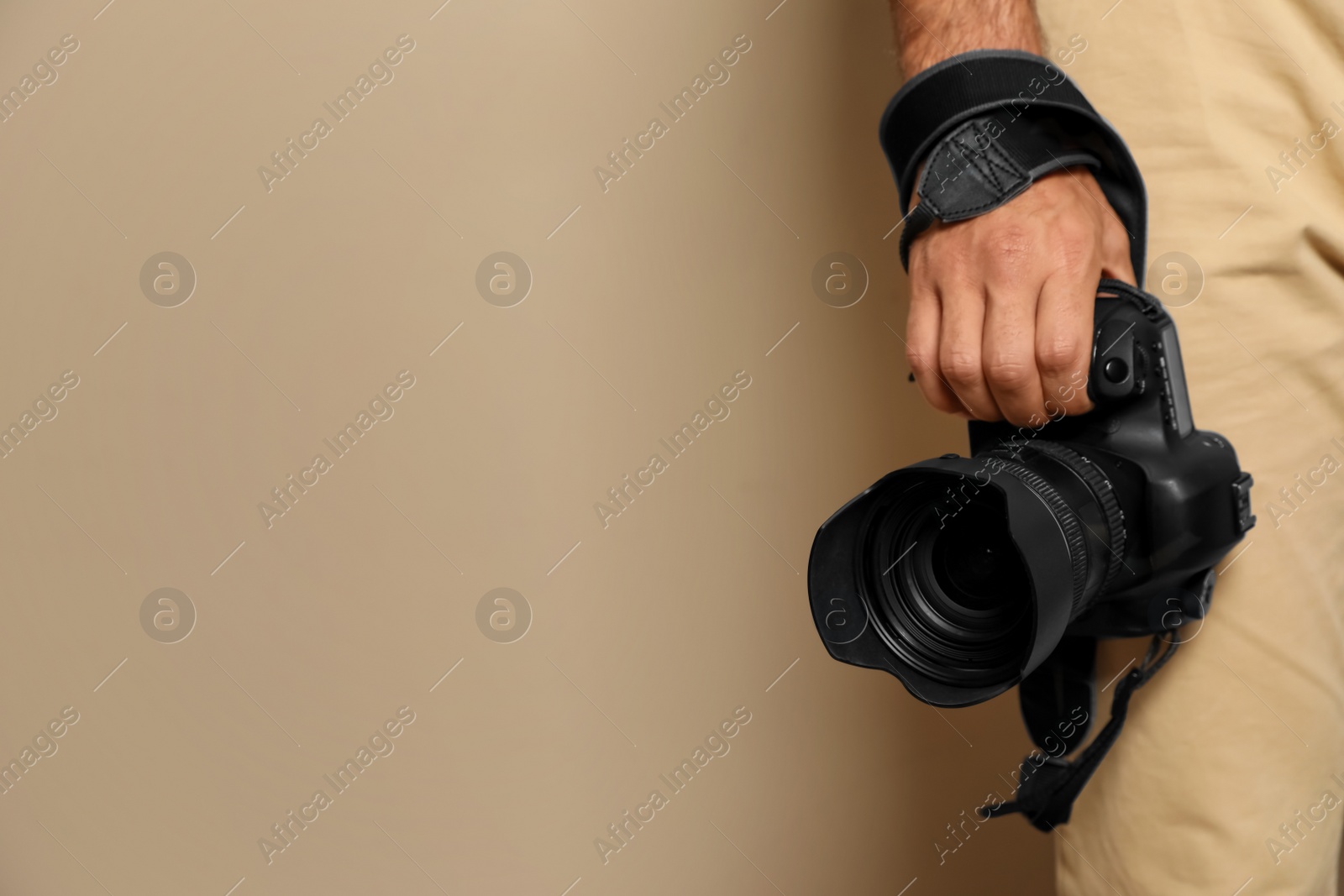 Photo of Professional photographer with modern camera on beige background in studio, closeup. Space for text