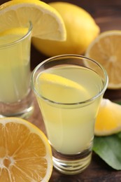 Photo of Tasty limoncello liqueur, lemons and green leaf on table, closeup