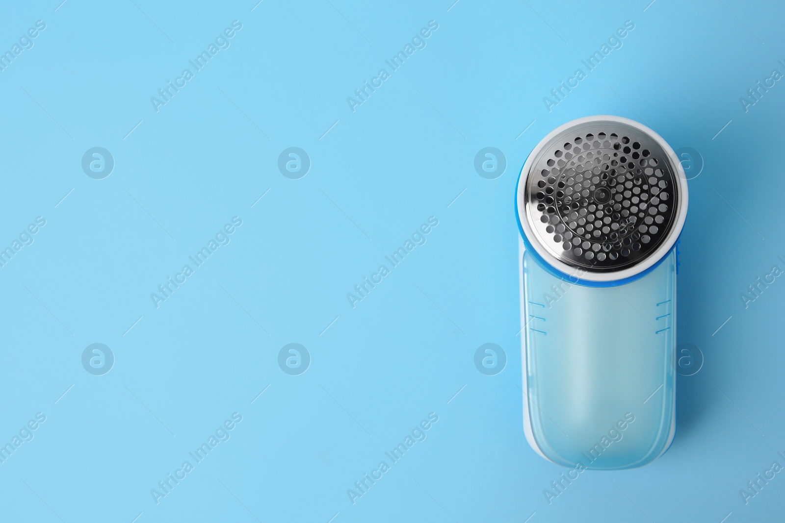 Photo of Modern fabric shaver on light blue background, top view. Space for text