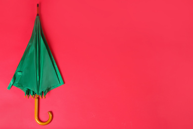 Beautiful green umbrella on red background, top view. Space for text