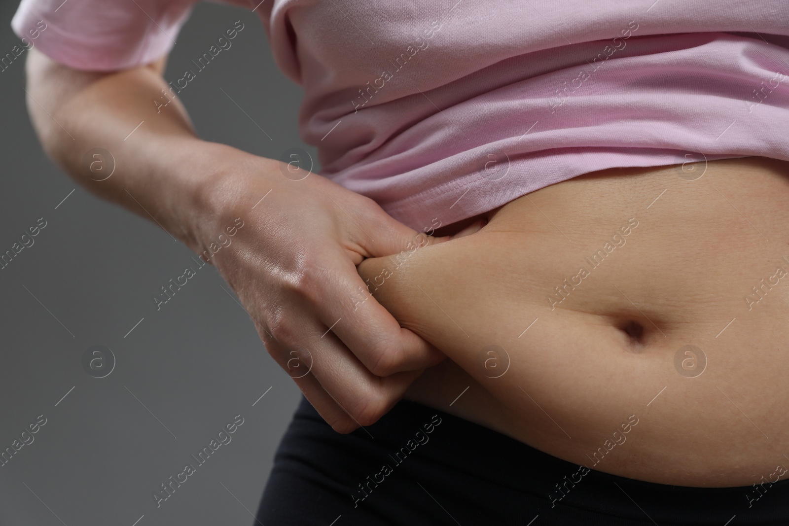 Photo of Woman touching belly fat on grey background, closeup. Overweight problem