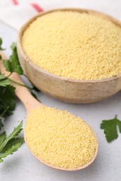 Raw couscous in bowl, spoon and parsley on light table, closeup