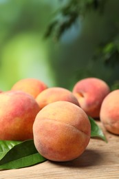 Photo of Fresh peaches and leaves on wooden table against blurred background, closeup. Space for text