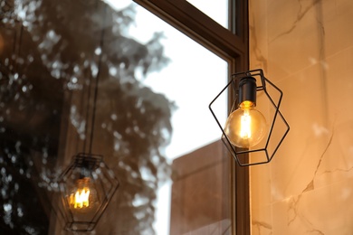 Photo of Pendant lamp with glowing light bulb near window indoors. Space for text