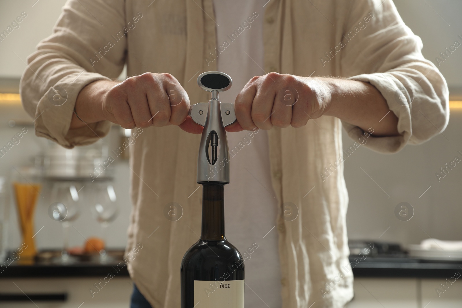 Photo of Man opening wine bottle with corkscrew in kitchen, closeup