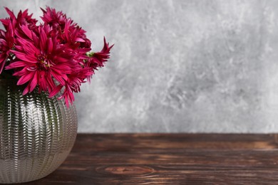 Beautiful pink chrysanthemum flowers in glass vase on wooden table. Space for text