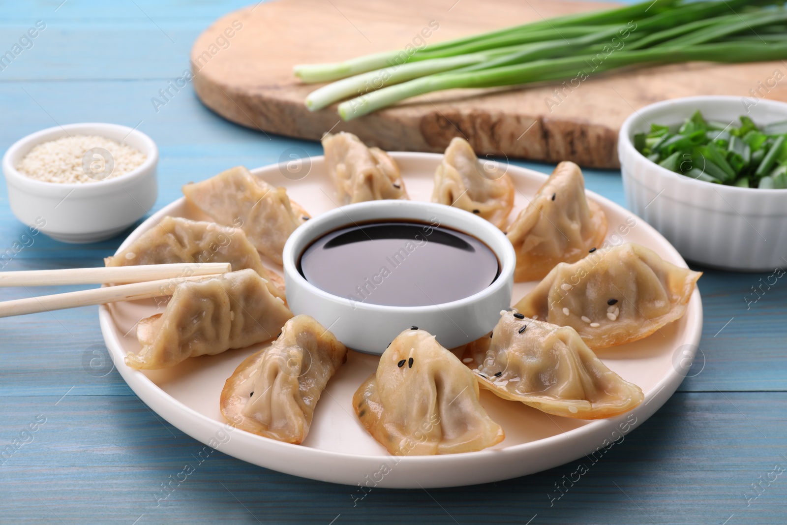 Photo of Delicious gyoza (asian dumplings), soy sauce and chopsticks on light blue wooden table, closeup