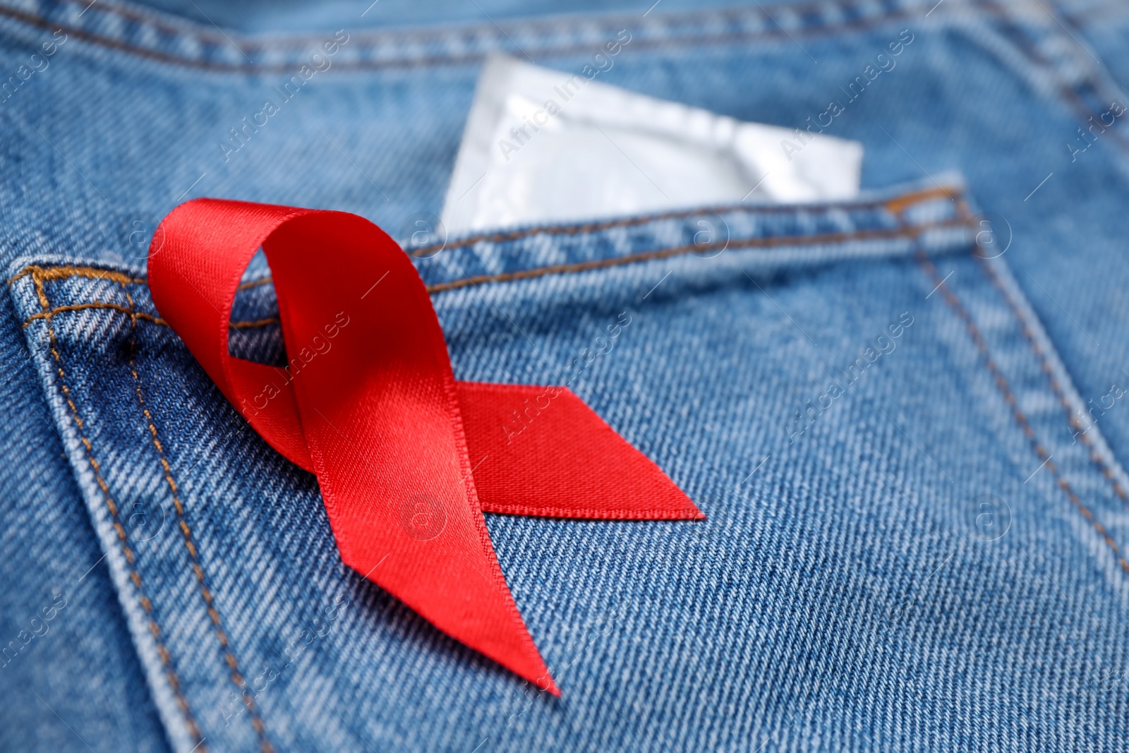 Photo of Jeans with red ribbon and condom, closeup. AIDS disease awareness