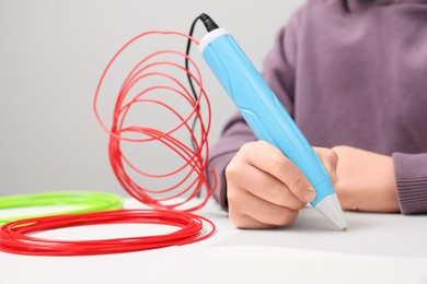 Photo of Boy drawing with stylish 3D pen at white table, closeup