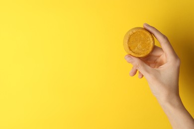 Woman holding orange solid shampoo bar against yellow background, closeup. Space for text