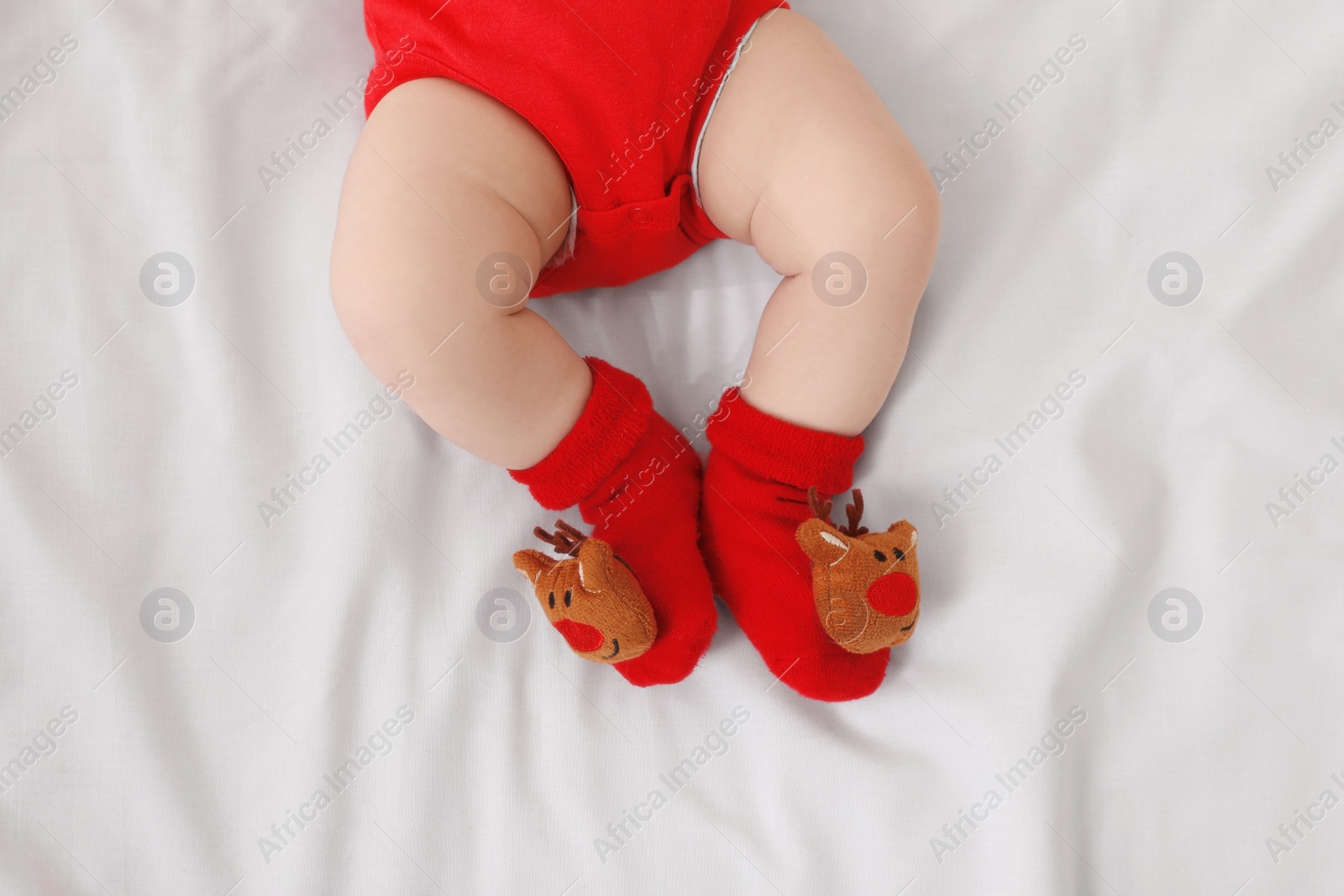 Photo of Baby wearing festive Christmas socks on white bedsheet, top view