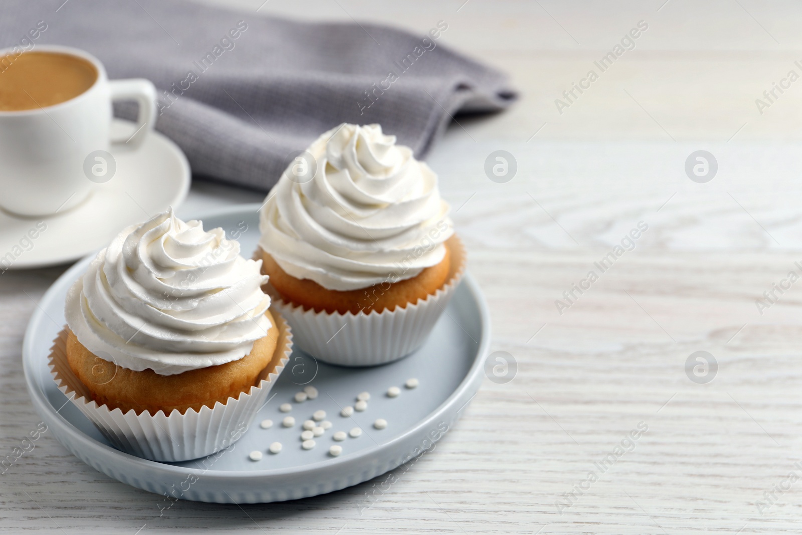 Photo of Delicious cupcakes with cream and cup of coffee on white wooden table. Space for text