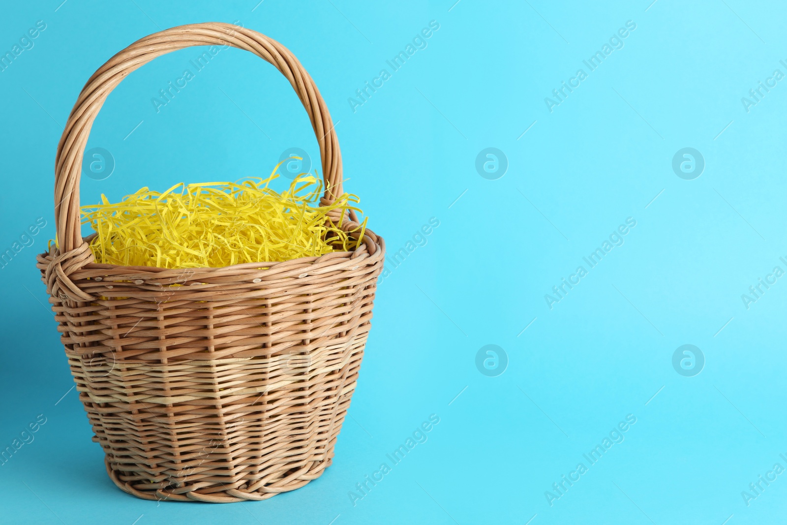 Photo of Easter basket with yellow paper filler on light blue background, space for text