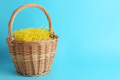 Photo of Easter basket with yellow paper filler on light blue background, space for text
