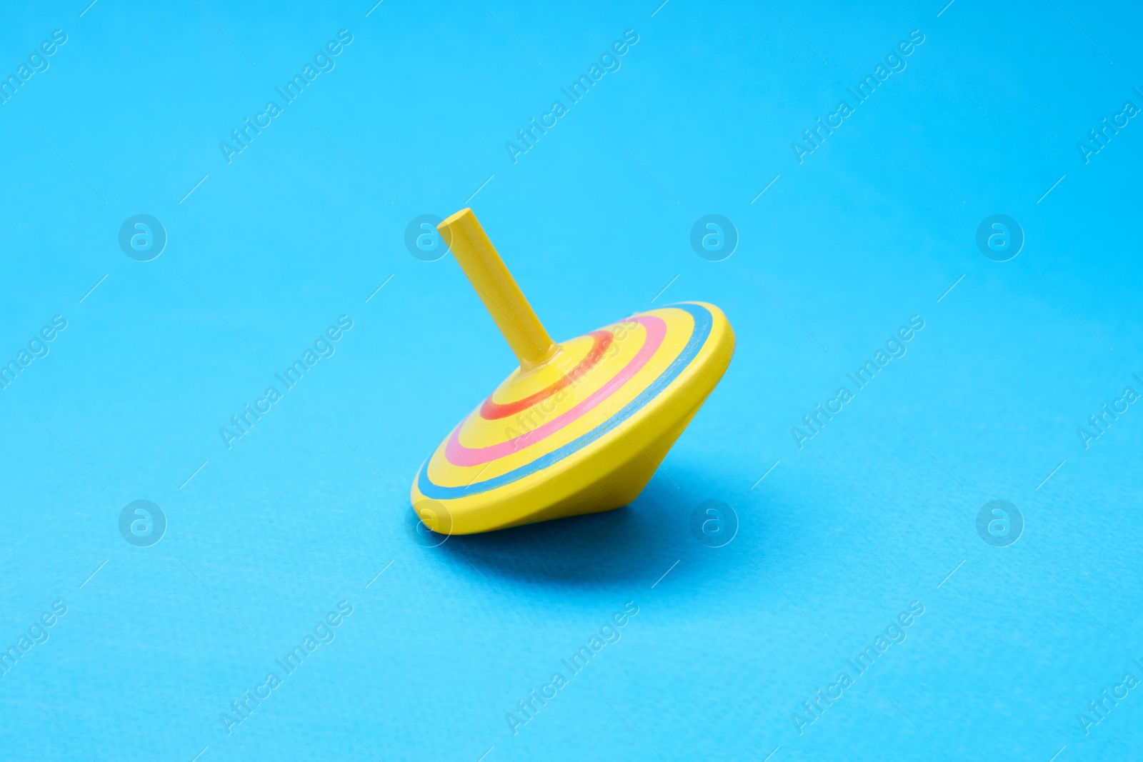 Photo of One bright spinning top on light blue background. Toy whirligig