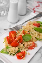 Delicious quinoa salad with tomatoes, beans and spinach leaves served on white marble table