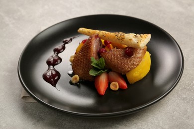 Photo of Plate with delicious chicken, parsnip and strawberries on grey table. Food stylist
