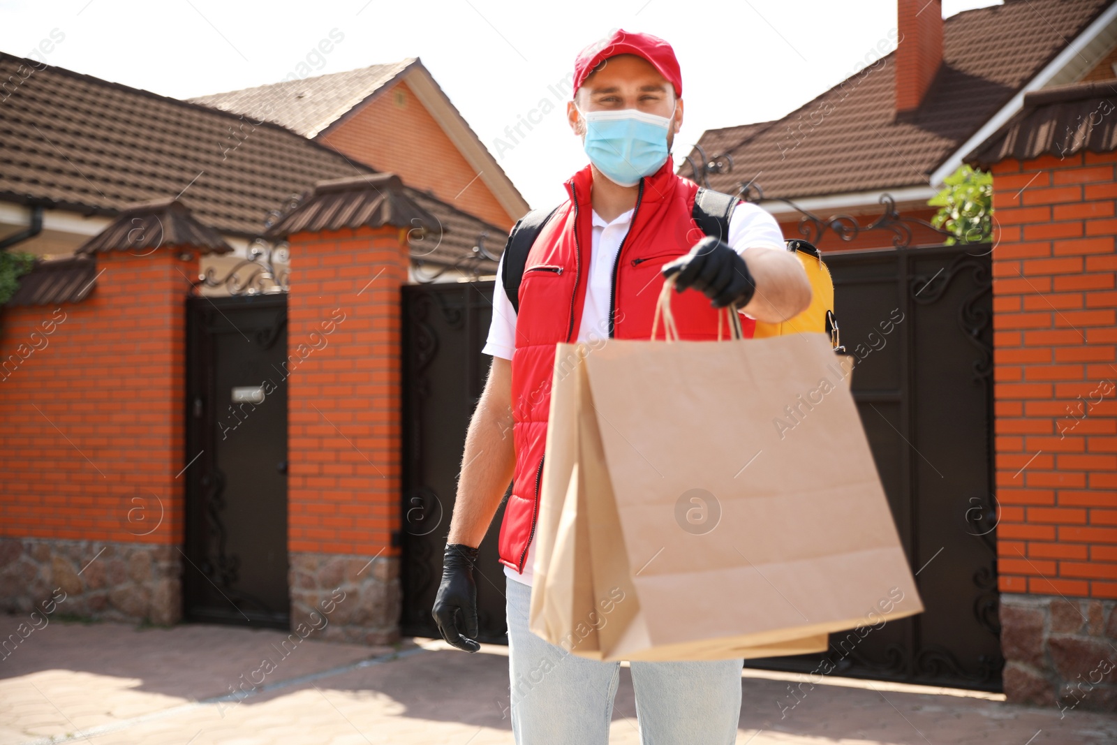 Photo of Courier in protective mask and gloves with order outdoors. Restaurant delivery service during coronavirus quarantine