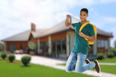 Image of Happy African American teenage boy jumping near house, space for text . School holidays