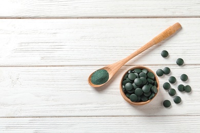 Photo of Bowl of spirulina pills and powder in spoon on wooden background, top view. Space for text