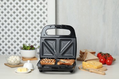 Modern grill maker with sandwiches and different products on white table