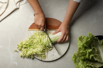 Woman cutting fresh Chinese cabbage at light grey table, top view