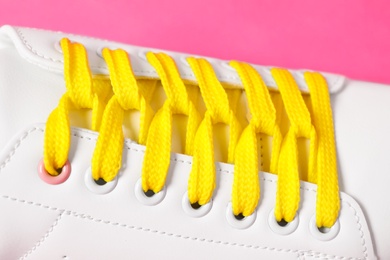 Stylish shoe with yellow laces on pink background, closeup