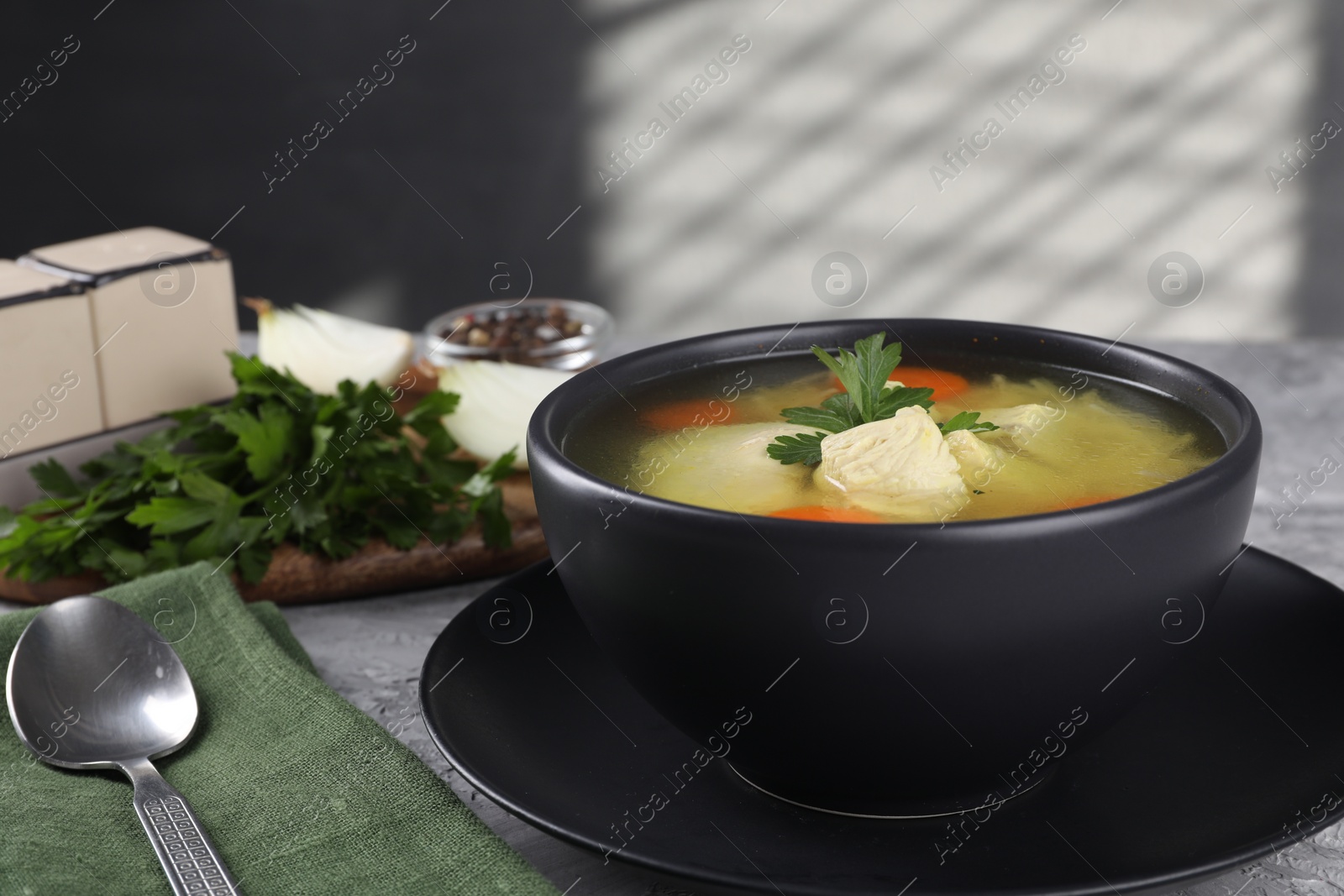 Photo of Tasty chicken soup with carrot and parsley in bowl served on grey textured table, closeup