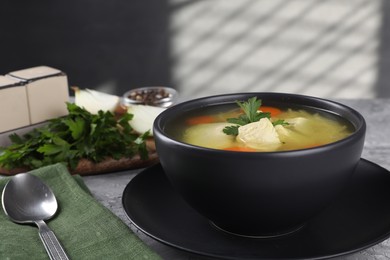 Tasty chicken soup with carrot and parsley in bowl served on grey textured table, closeup