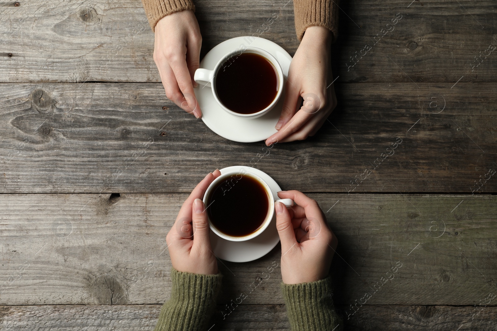 Photo of Women with cups of aromatic coffee at wooden table, top view