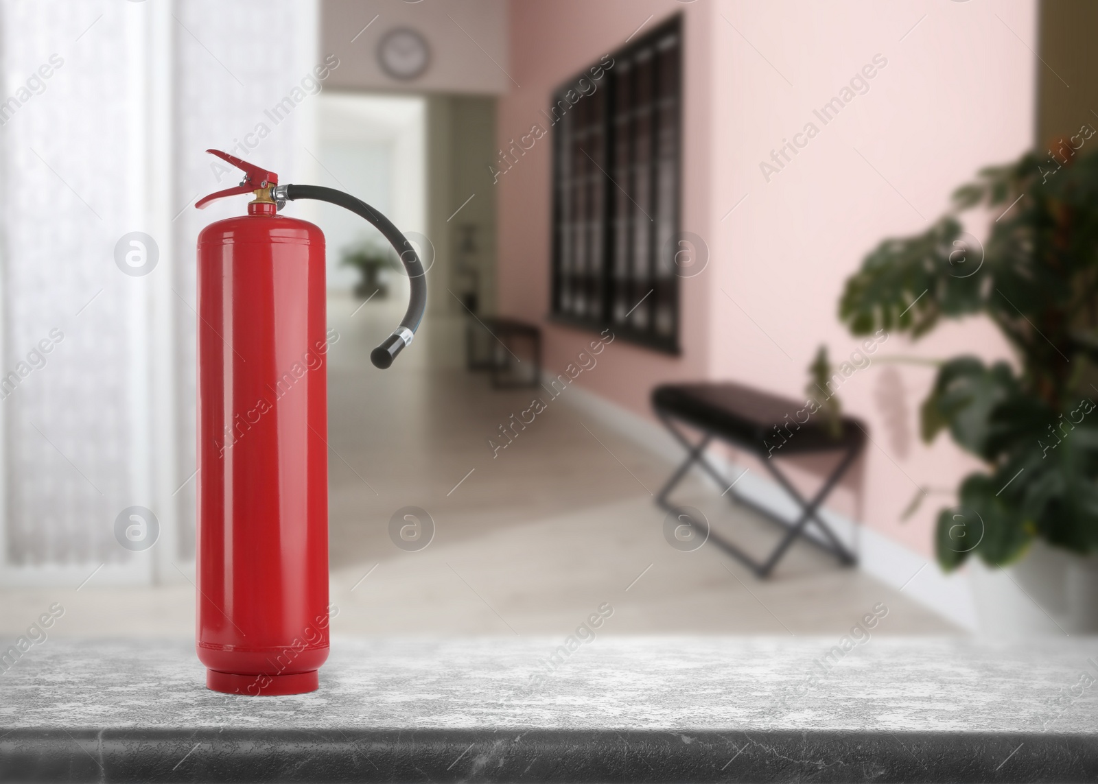 Image of Fire extinguisher on stone table in office corridor. Space for text