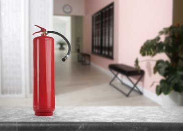 Image of Fire extinguisher on stone table in office corridor. Space for text