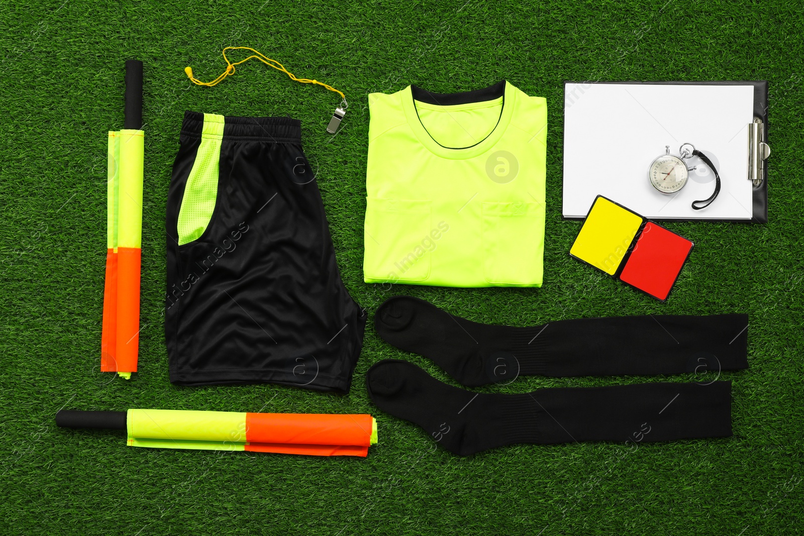 Photo of Uniform and other referee equipment on green grass, flat lay