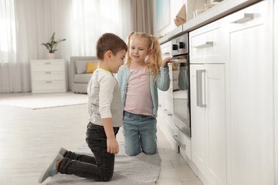 Photo of Little kids waiting for preparation of food in oven at home