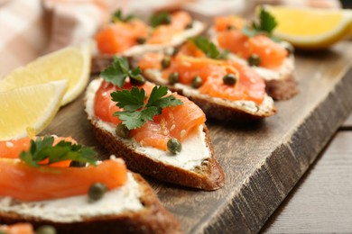 Photo of Tasty canapes with salmon, capers, lemon and cream cheese on wooden table, closeup