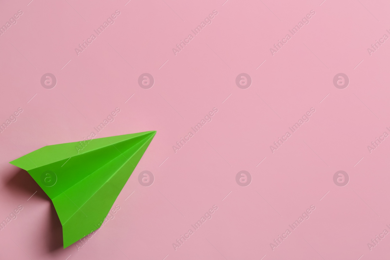 Photo of Green paper plane on pink background, top view. Space for text