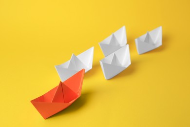 Group of paper boats following orange one on yellow background. Leadership concept