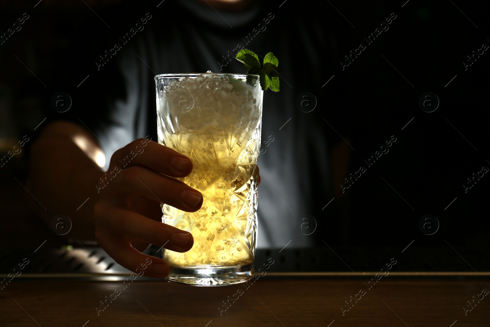 Photo of Bartender holding glass of fresh alcoholic cocktail at bar counter, closeup. Space for text