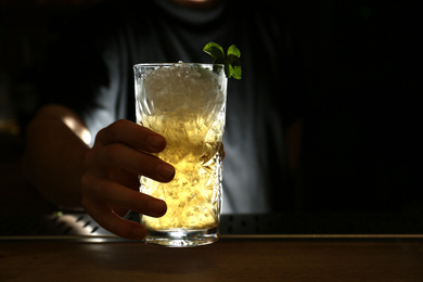 Bartender holding glass of fresh alcoholic cocktail at bar counter, closeup. Space for text
