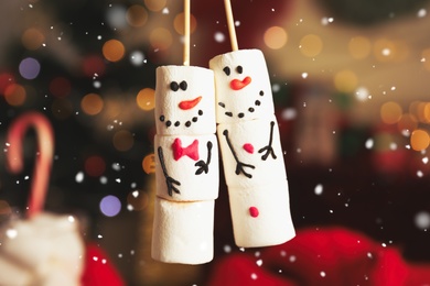 Funny snowmen made of marshmallows against blurred festive lights, closeup