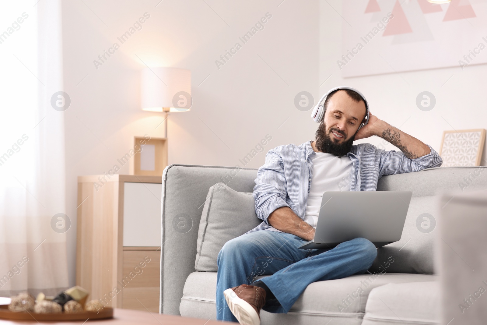 Photo of Mature man with headphones and laptop on sofa at home