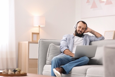 Mature man with headphones and laptop on sofa at home