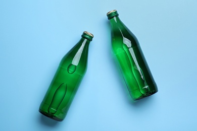 Photo of Glass bottles with water on light blue background, flat lay